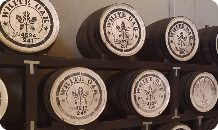 Rows of wooden barrels labeled 'White Oak' stacked on dark wooden racks in a storage area.