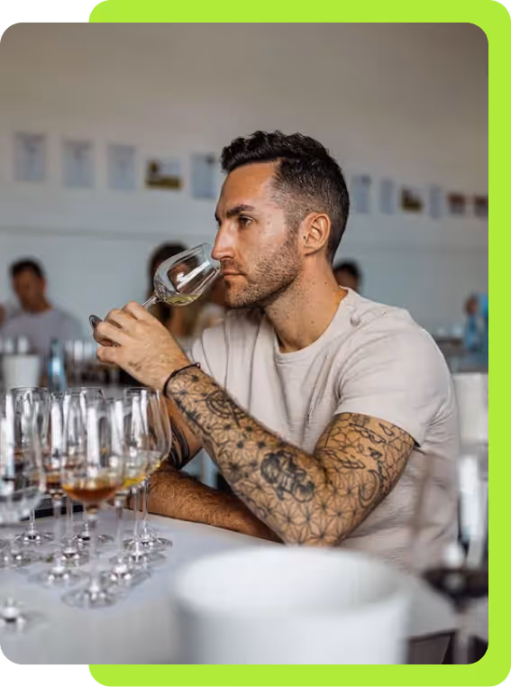 Man with tattooed arms smelling wine in a glass at a tasting event.