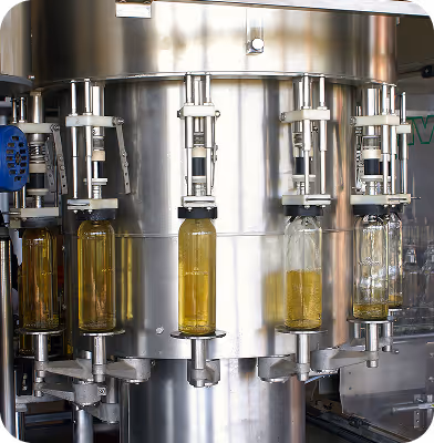 Industrial machine filling glass bottles with a yellow liquid in a bottling facility.