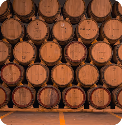 Stacked wooden barrels stored in rows inside a warehouse or cellar.