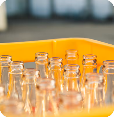 Empty clear glass bottles placed inside a yellow plastic crate.