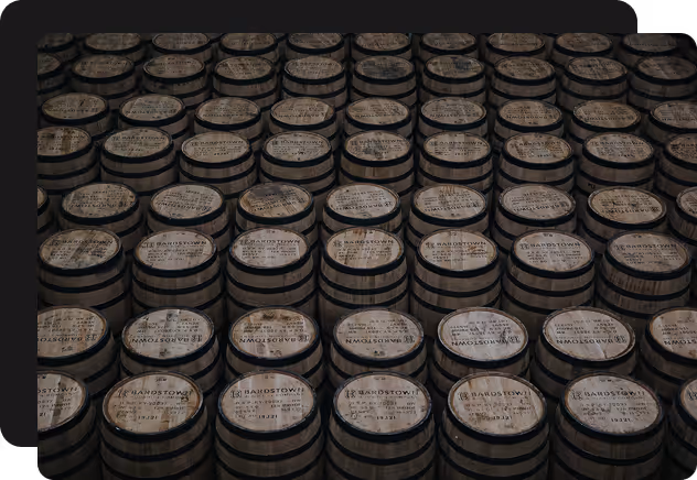 Rows of wooden barrels labeled Bardstown stacked closely together under dim lighting.