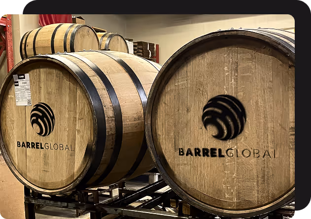 Wooden barrels with black metal bands, labeled 'BARREL GLOBAL', stacked on a metal rack in a storage area.