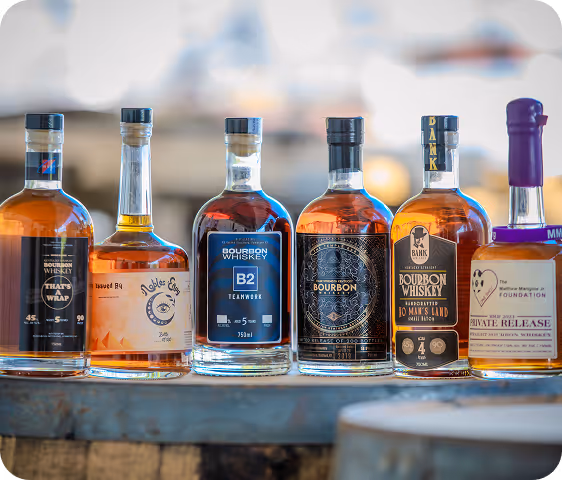 Six bottles of bourbon whiskey lined up on a wooden surface with blurred background.