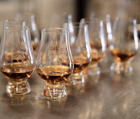 Rows of whiskey tasting glasses with amber liquid on a reflective surface.