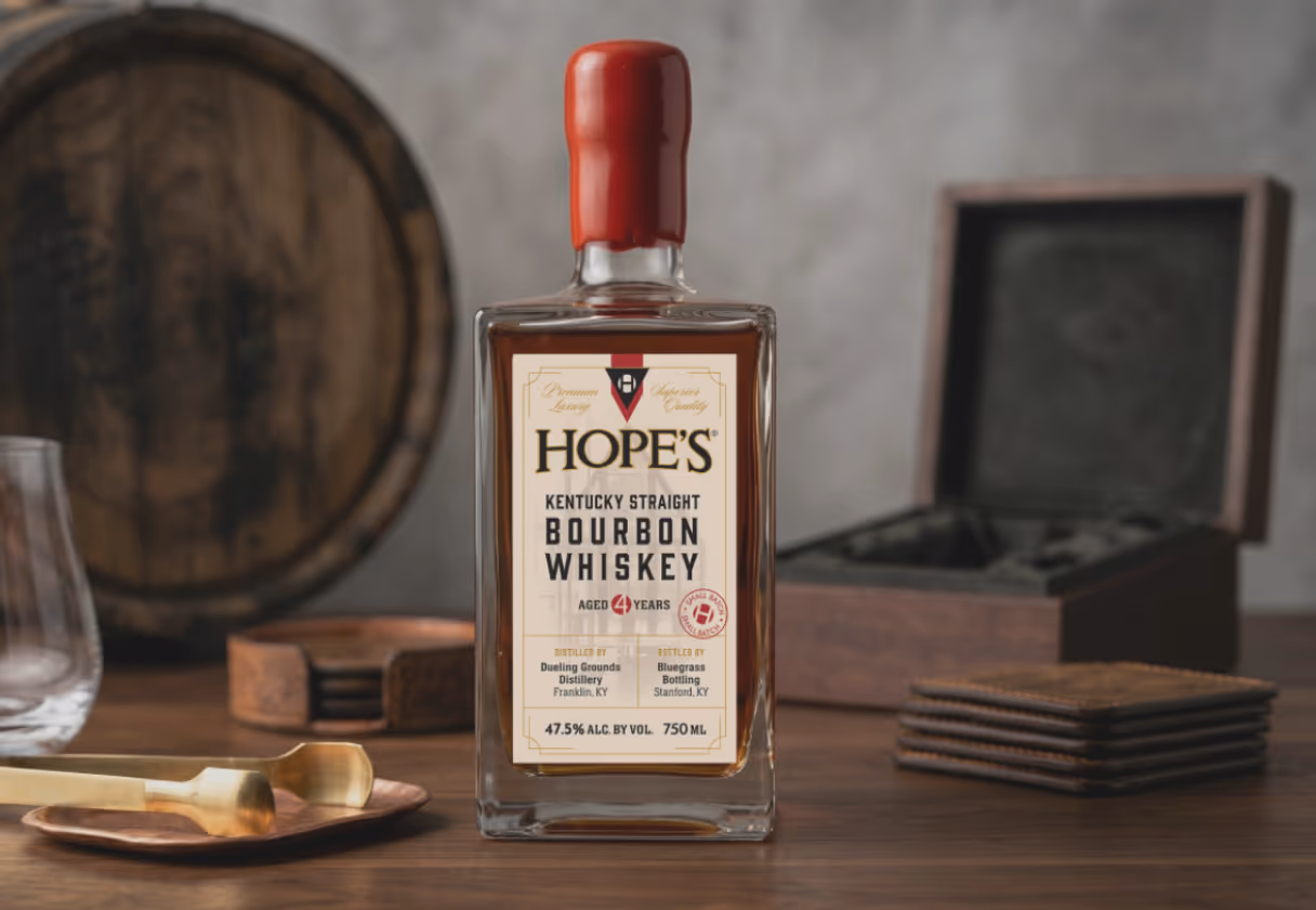 Bottle of Hope's Kentucky Straight Bourbon Whiskey aged 4 years, 47.5% alcohol, on a wooden table with a glass, whiskey tools, coasters, and a wooden box.