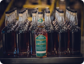 Rows of glass bottles filled with amber liquid, one bottle in front with a green and gold label reading "Aged Bar Premium Reserve".