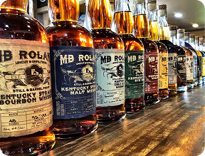 Row of various bourbon whiskey bottles displayed on a wooden counter.