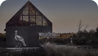 Wild Turkey Distillery building with a turkey logo at dusk surrounded by grass and trees.