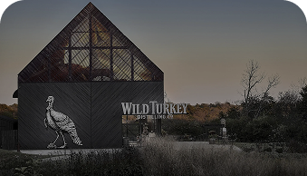 Wild Turkey Distillery building with a turkey logo at dusk surrounded by grass and trees.