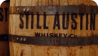 Wooden whiskey barrel with metal bands labeled Still Austin Whiskey Co.