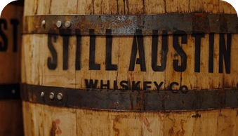 Wooden whiskey barrel with metal bands labeled Still Austin Whiskey Co.