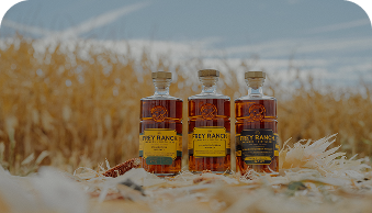 Three bottles of Frey Ranch whiskey on grass with a field and blue sky background.