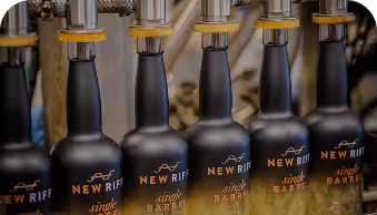 Row of black New Riff single barrel bottles lined up on a tap system.