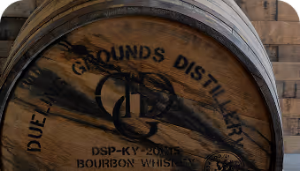 Wooden barrel labeled New Grounds Distillery Bourbon Whiskey with a rustic wood background.