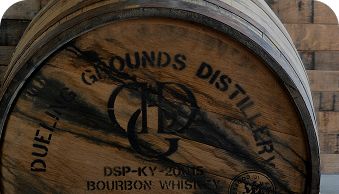 Wooden barrel labeled New Grounds Distillery Bourbon Whiskey with a rustic wood background.