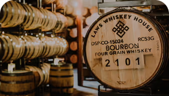Close-up of bourbon barrel labeled Four Grain Whiskey in a warehouse with stacked barrels.