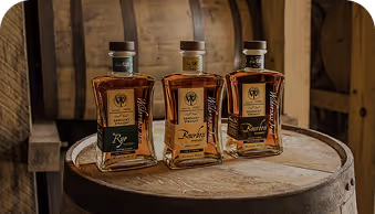 Three rectangular whiskey bottles on a wooden barrel in front of large wooden barrels.