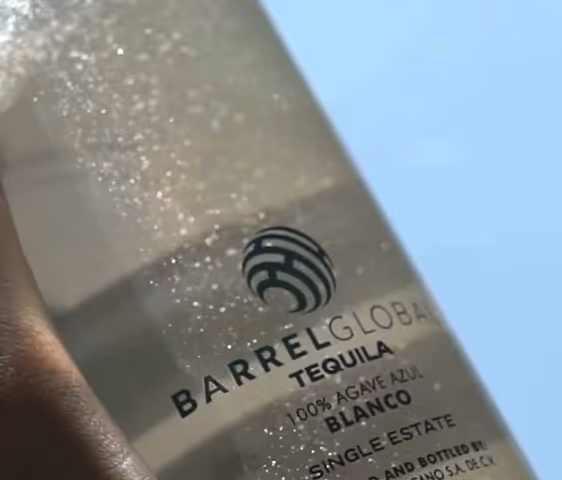 Close-up of Barrel Global tequila blanco bottle with 100% agave azul and sparkles on glass.