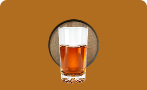 Glass of amber liquid with an ice cube on a brown surface with circular wood texture behind.