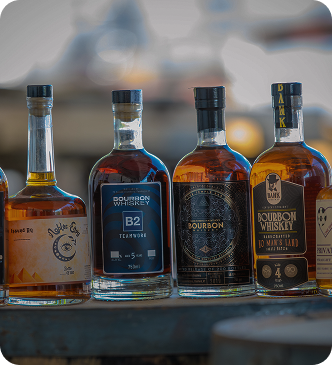 Four bottles of bourbon whiskey lined up on a rustic wooden surface with blurred background.