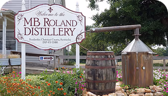 Sign welcoming visitors to MB Roland Distillery in Pembroke, Kentucky with barrels and copper distiller.