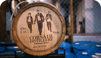 Wooden barrel with Corsair Distillery logo showing three men in suits inside a distillery warehouse.