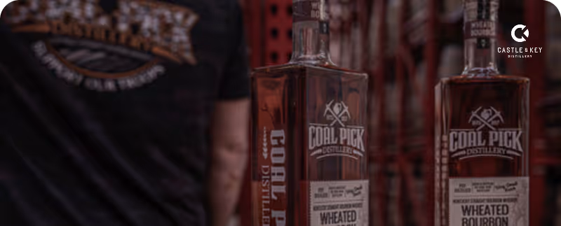 Two bottles of Coal Pick Distillery Wheated Bourbon in front of a person wearing a Coal Pick t-shirt.