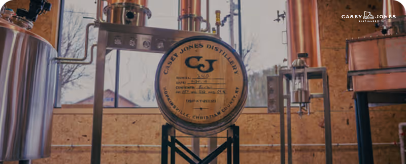 Wooden barrel labeled Casey Jones Distillery surrounded by distillation equipment inside a workshop.