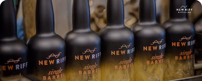 Row of matte black New Riff Single Barrel whiskey bottles with gold lettering displayed.