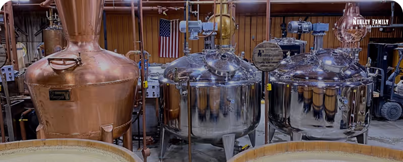 Copper and steel distillation tanks in a distillery with an American flag and wooden barrels.