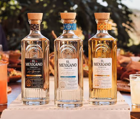 Three El Mexicano tequila bottles with wooden caps on a table outdoors with blurred background.