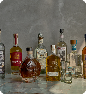 Various liquor bottles placed on a tiled surface with two shot glasses beside them.