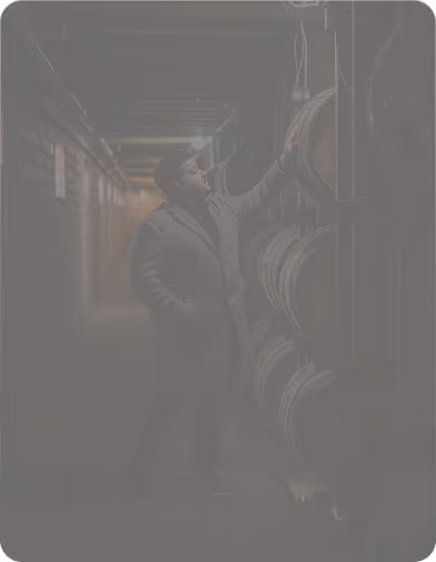 Man inspecting wooden barrels in a dimly lit cellar or storage room.
