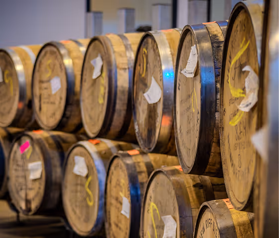 Rows of wooden barrels with tags and yellow markings stacked in a cellar or storage area.