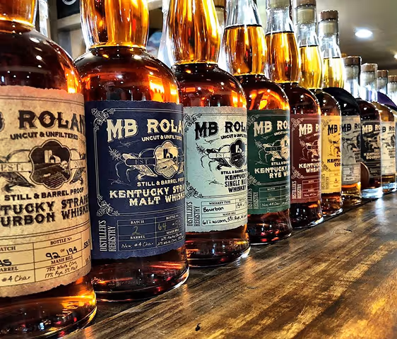 Row of MB Roland whiskey bottles in different varieties lined up on a wooden surface.