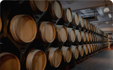 Rows of wooden barrels stacked on racks inside a dimly lit aging warehouse.