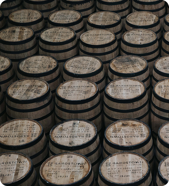 Rows of wooden barrels labeled Bardstown, stacked tightly in a warehouse.
