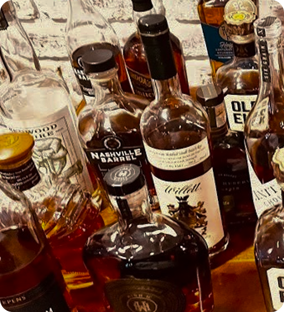 Various whiskey bottles grouped together on a wooden surface against a white brick wall.