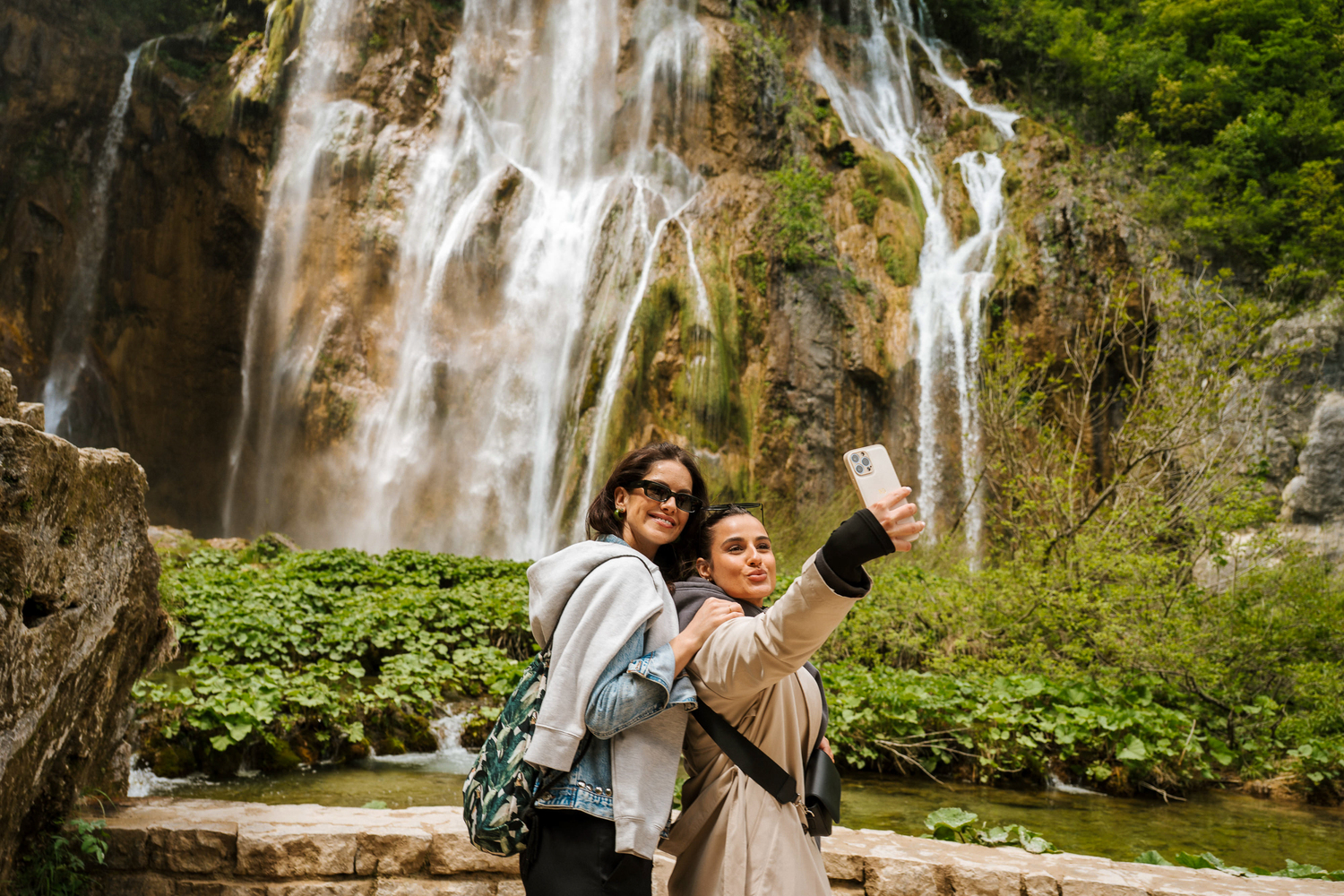 Two tourists taking selfies by the waterfalls of Plitvice Lakes National Park