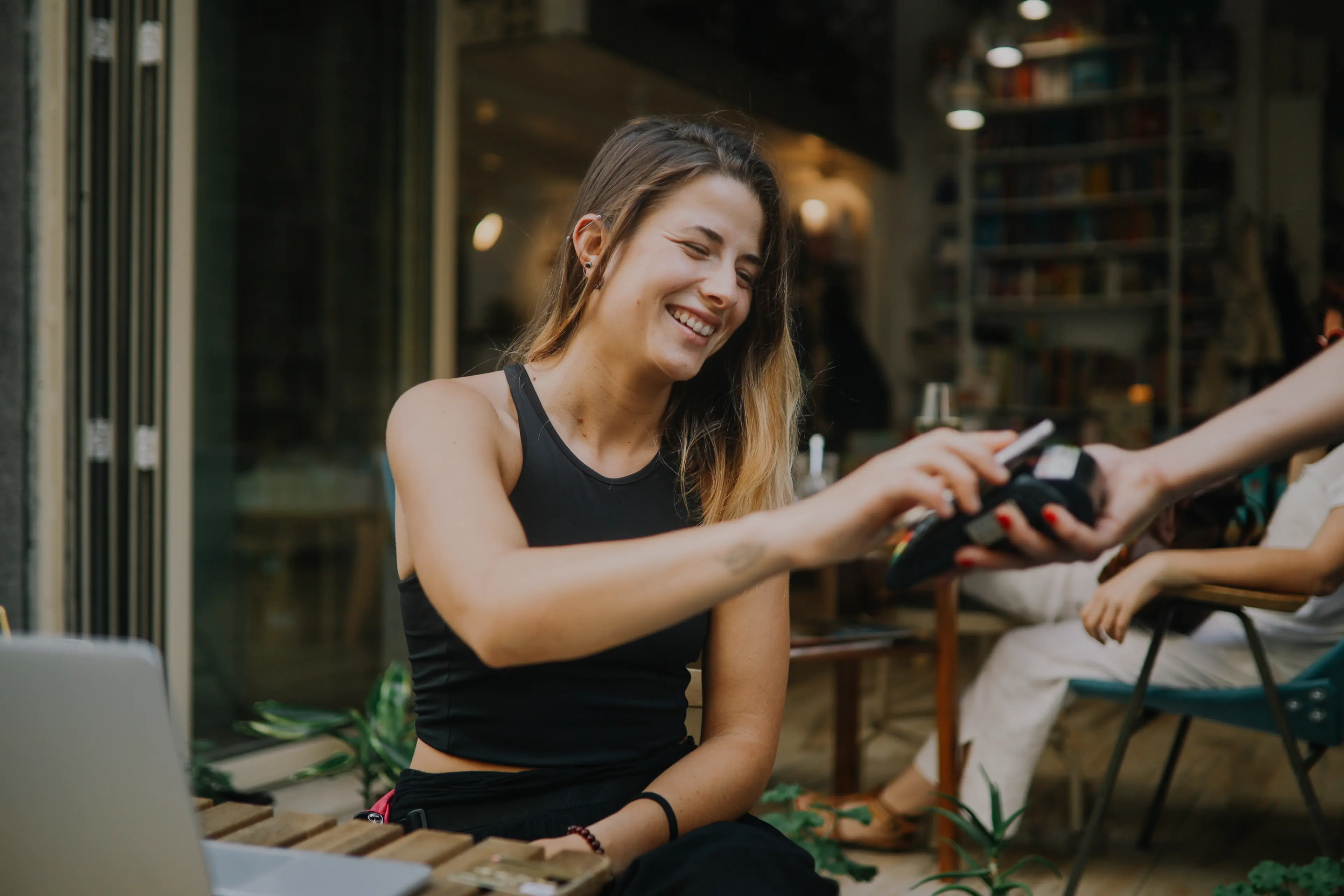 Smiling woman in a black tank top making a payment with a card using a wireless card reader.