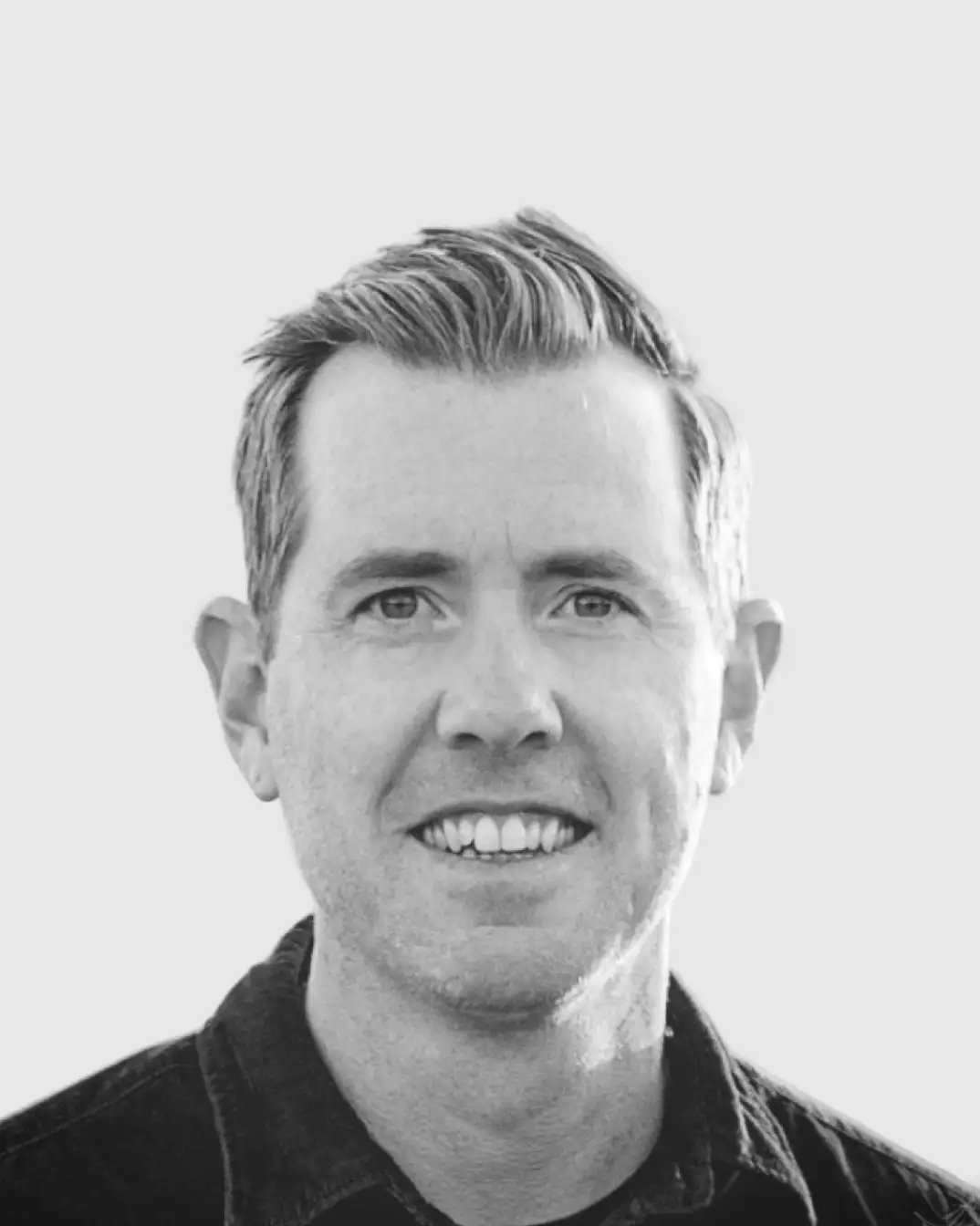 Black and white portrait of a smiling middle-aged man with short, styled hair wearing a dark collared shirt.
