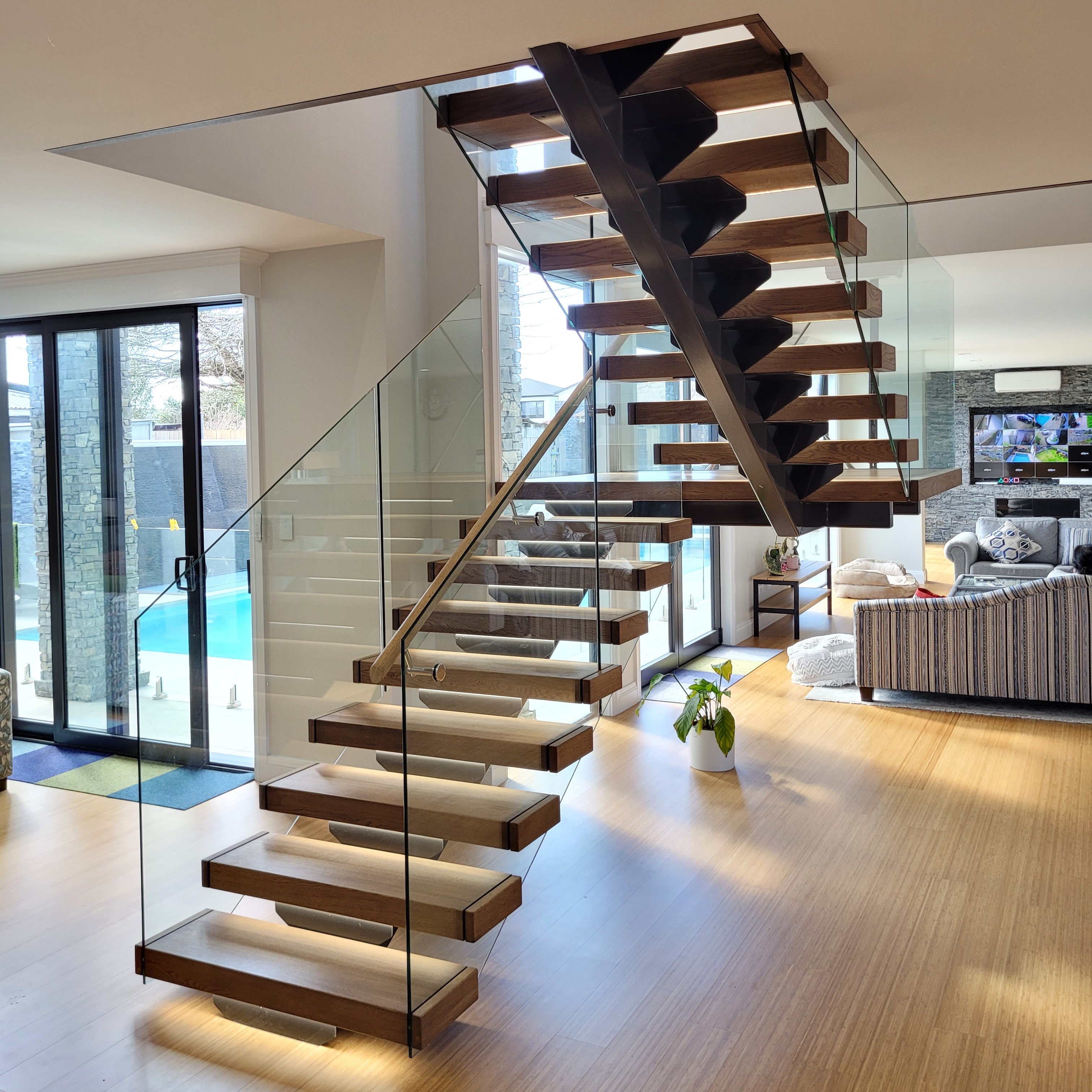 Minimalist floating stairs with timber treads and LED strip lighting underneath and glass balustrades 