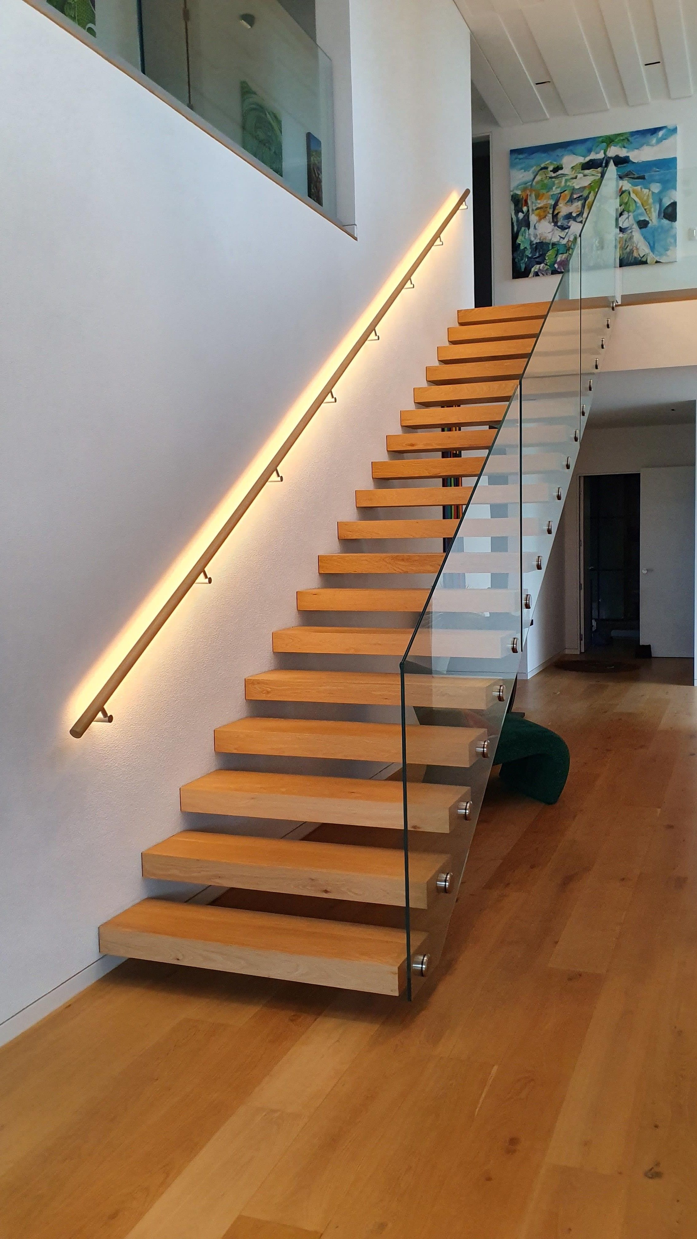 A modern interior in this residential property features a floating wooden staircase, glass balustrade and timber handrail with LED lighting rebated in.