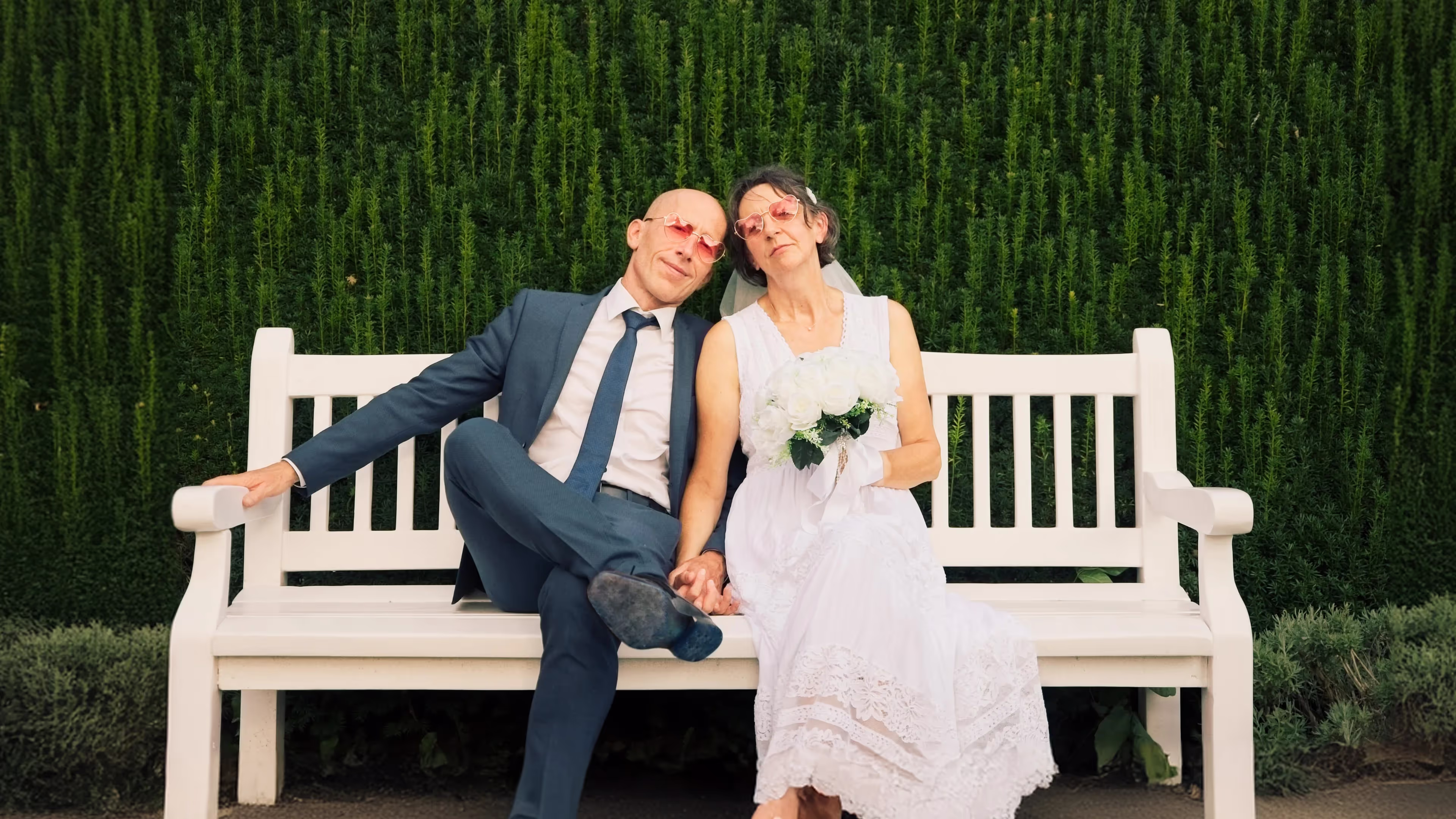 Bride and groom sitting on a white bench