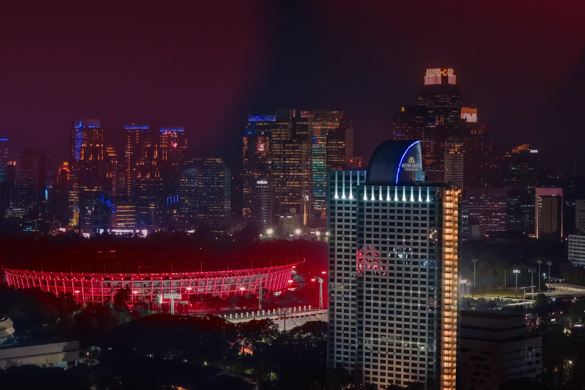 Hotel Mulia Senayan illuminated against Jakarta's night skyline, overlooking the stadium and promoting the Stay Close to the Concert package.