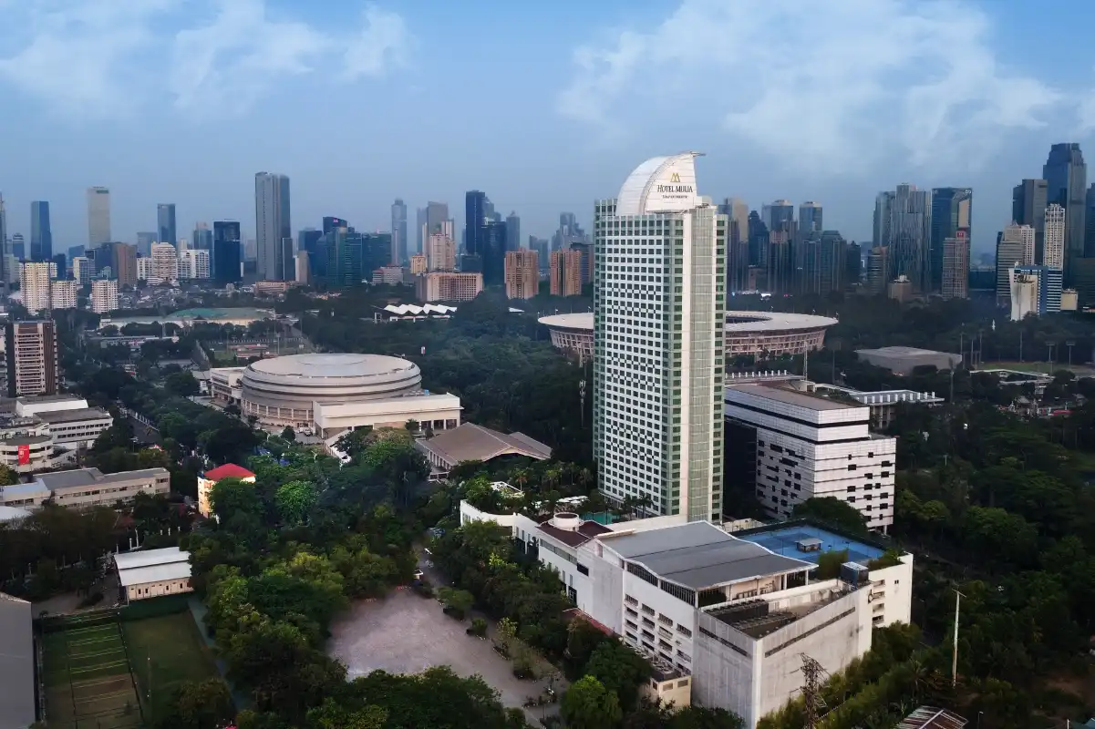 Aerial view of a luxury hotel tower at dusk overlooking the city skyline, promoting an open-air to indoor meetings package.