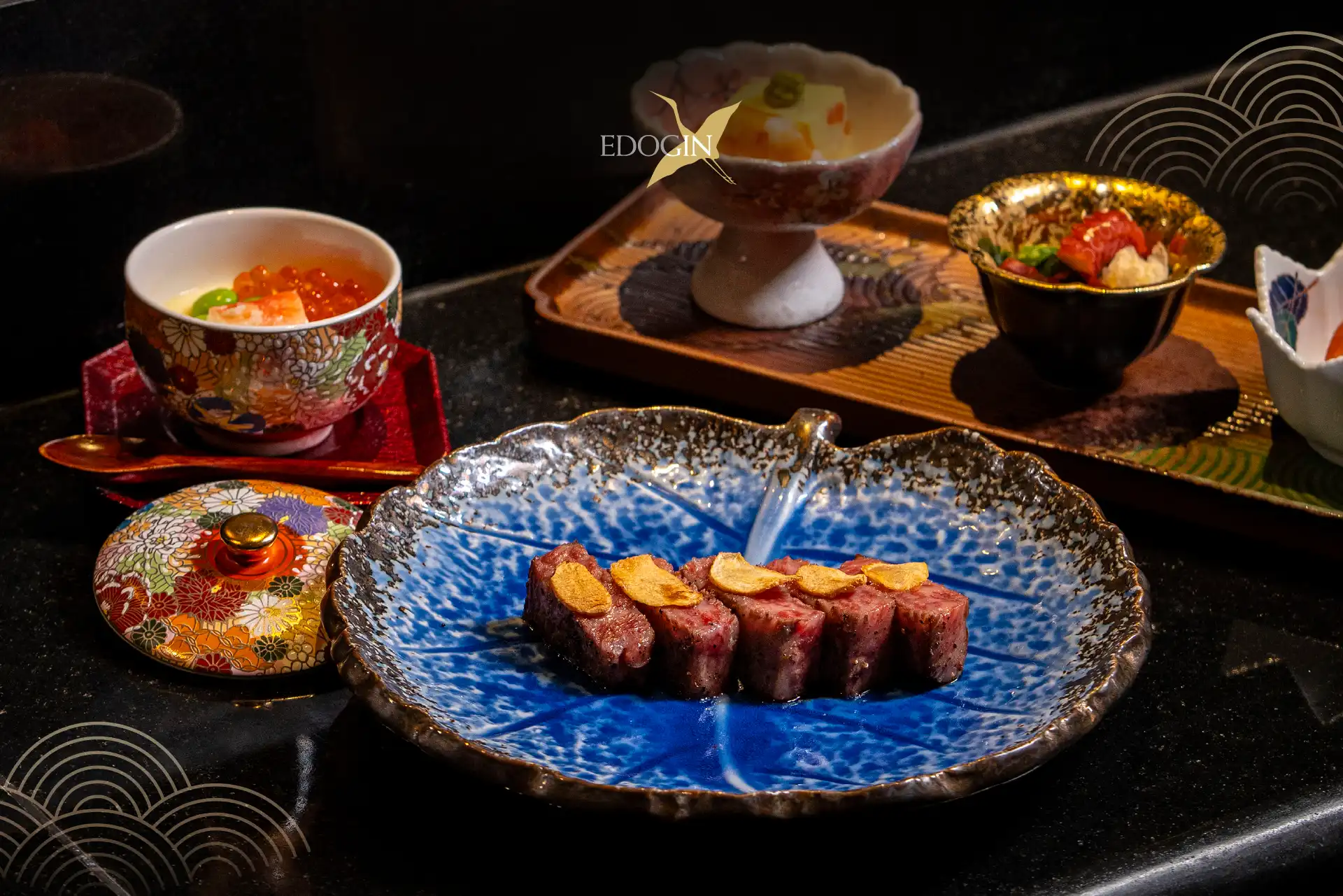 Sliced grilled wagyu beef with garlic chips on a decorative blue ceramic plate, part of the Edogin Teppanyaki dining experience.