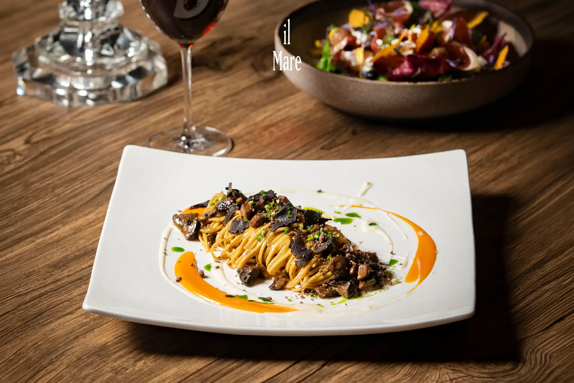 Truffle Tagliolini on a white plate with a Spinach & Radicchio Salad and a glass of red wine, part of the Autumn at il Mare seasonal menu, Hotel Mulia SenayanJakarta.