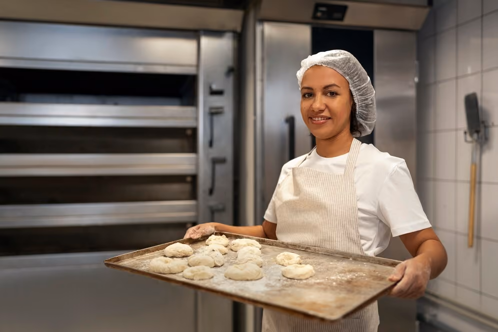 Woman holding a baking tray with freshly prepared dough in a bakery